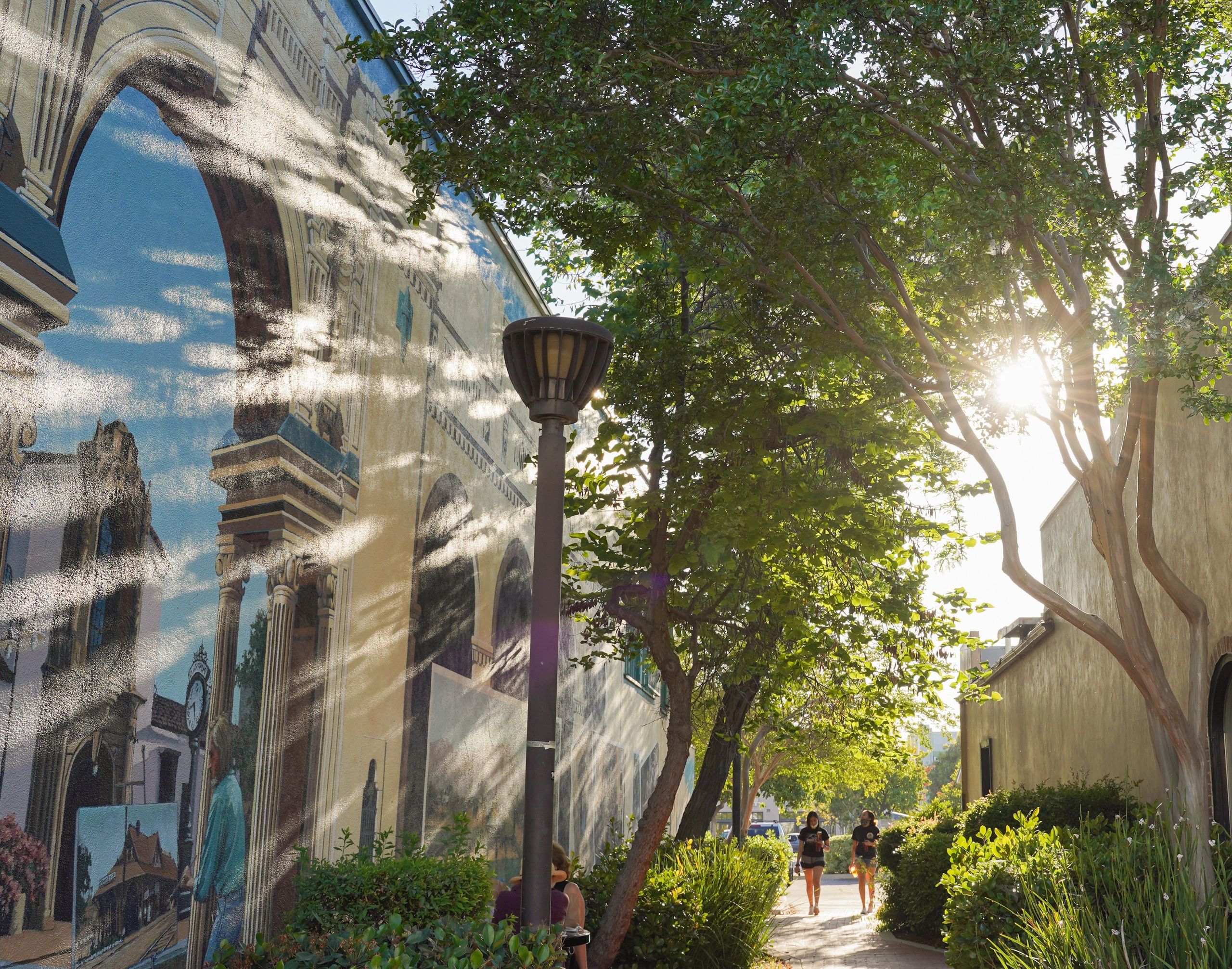 Tree-shaded walkway beside a mural in Claremont Village